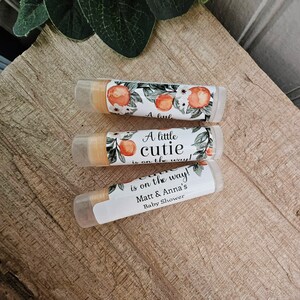 May include: Three lip balm tubes with a floral design and the text "A little cutie is on the way!" and "Matt & Anna's Baby Shower".