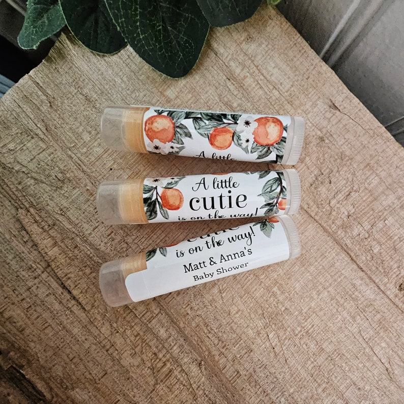 May include: Three lip balm tubes with a floral design and the text "A little cutie is on the way!" and "Matt & Anna's Baby Shower".