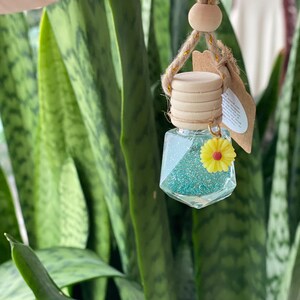 May include: A teal blue glass car air freshener with glitter and a yellow flower charm hanging from a brown rope with a wooden bead.