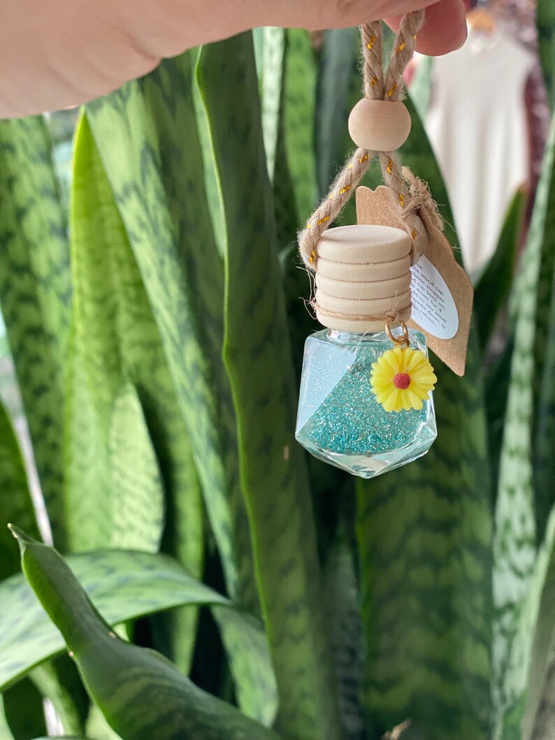 May include: A teal blue glass car air freshener with glitter and a yellow flower charm hanging from a brown rope with a wooden bead.