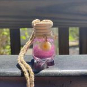 May include: A small glass bottle with a star-shaped base filled with pink glitter and a small yellow stone charm. The bottle is hanging from a brown cord.