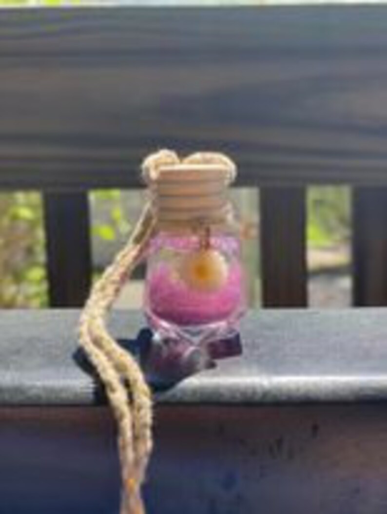 May include: A small glass bottle with a star-shaped base filled with pink glitter and a small yellow stone charm. The bottle is hanging from a brown cord.
