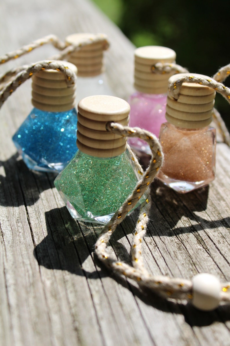 May include: Four small glass bottles with cork tops filled with glitter. The bottles are hanging from a string with a wooden bead at the end. The glitter is blue, green, pink, and brown.