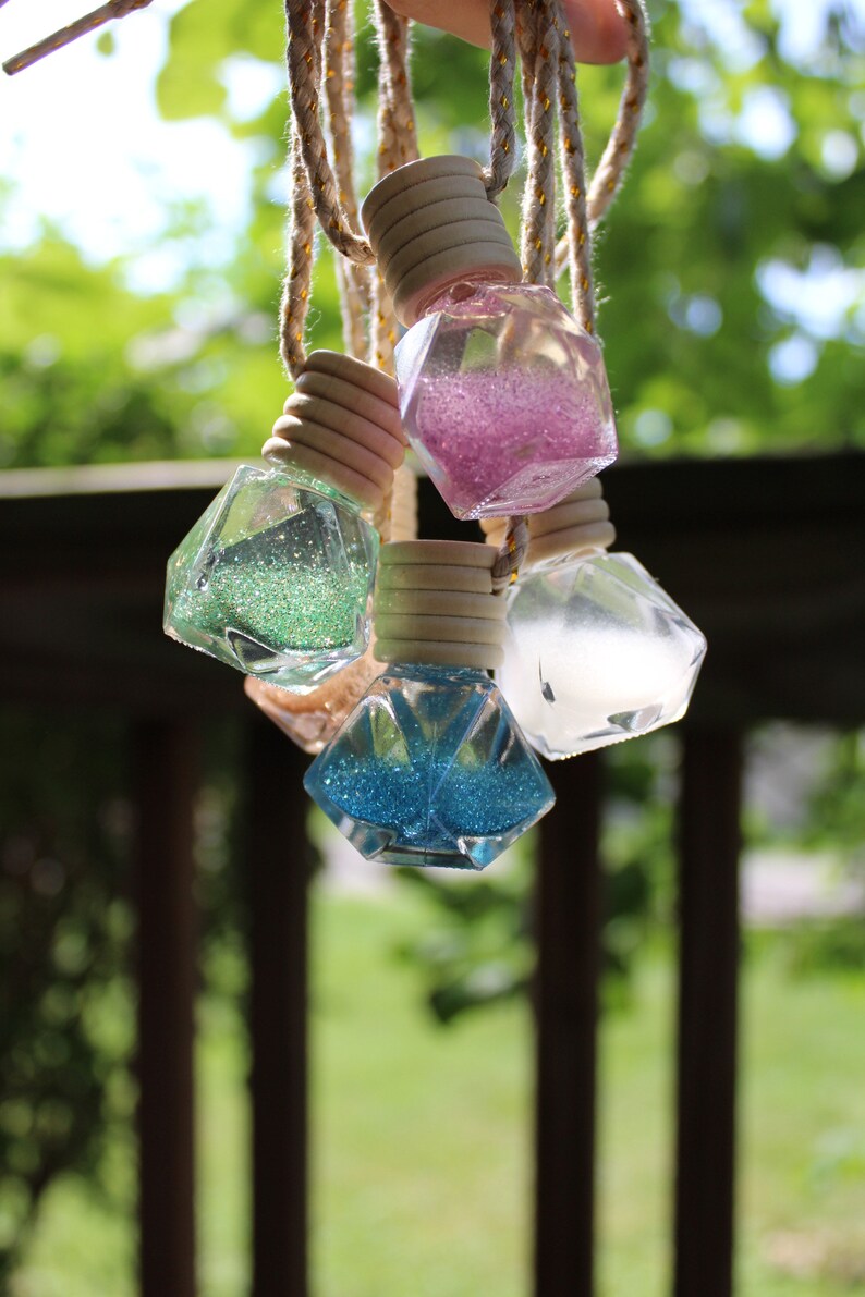 May include: Five decorative glass bottles with glitter inside, hanging from twine cords. The bottles are shaped like diamonds and come in pink, green, blue, and clear.
