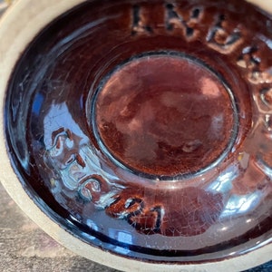 May include: Close-up of the bottom of a brown ceramic mug with a brown glaze. The mug has a crackled glaze and the words "Stoneware" are visible on the bottom.