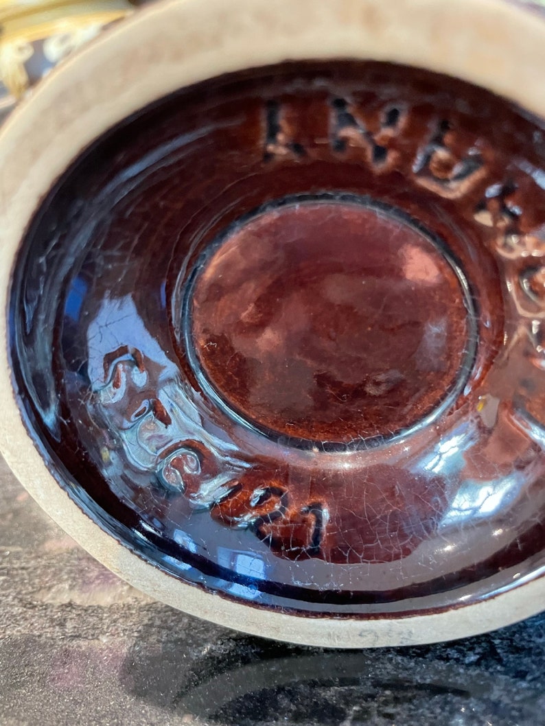 May include: Close-up of the bottom of a brown ceramic mug with a brown glaze. The mug has a crackled glaze and the words "Stoneware" are visible on the bottom.