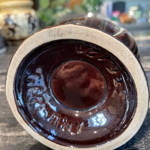 May include: A brown ceramic vase with a white rim and a brown glaze. The bottom of the vase has a white circle with the text "Germany" in black.