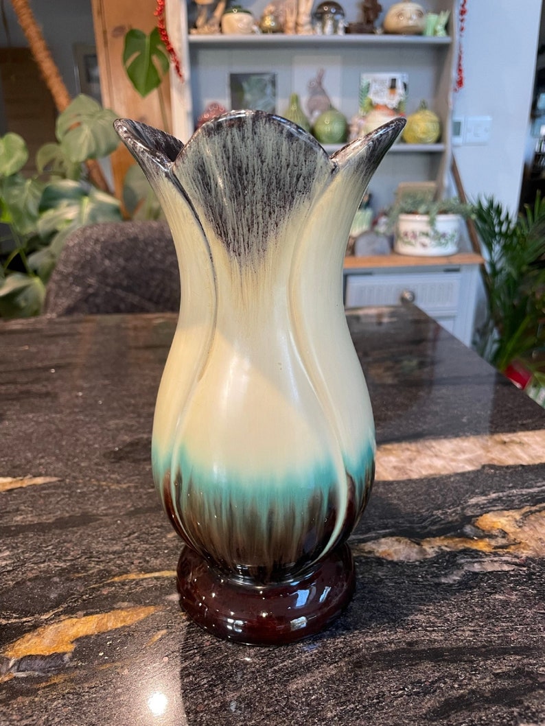May include: A ceramic vase with a tulip shape, featuring a cream base with brown and teal glaze. The vase has a wide mouth and a narrow base.