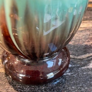 May include: A ceramic vase with a brown and green glaze. The vase has a rounded body and a wide base.