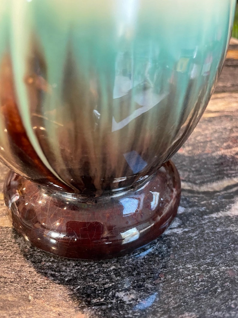 May include: A ceramic vase with a brown and green glaze. The vase has a rounded body and a wide base.