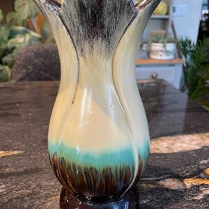 May include: A ceramic vase with a tulip-shaped design. The vase is decorated with a brown, white, and blue glaze. The vase has a wide mouth and a narrow base.