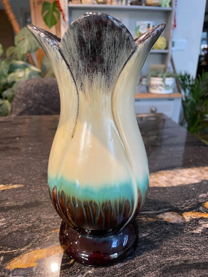 May include: A ceramic vase with a tulip-shaped design. The vase is decorated with a brown, white, and blue glaze. The vase has a wide mouth and a narrow base.