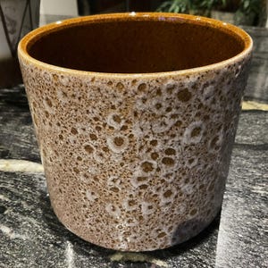 May include: A brown ceramic planter with a speckled white glaze. The planter has a round shape and a wide opening.