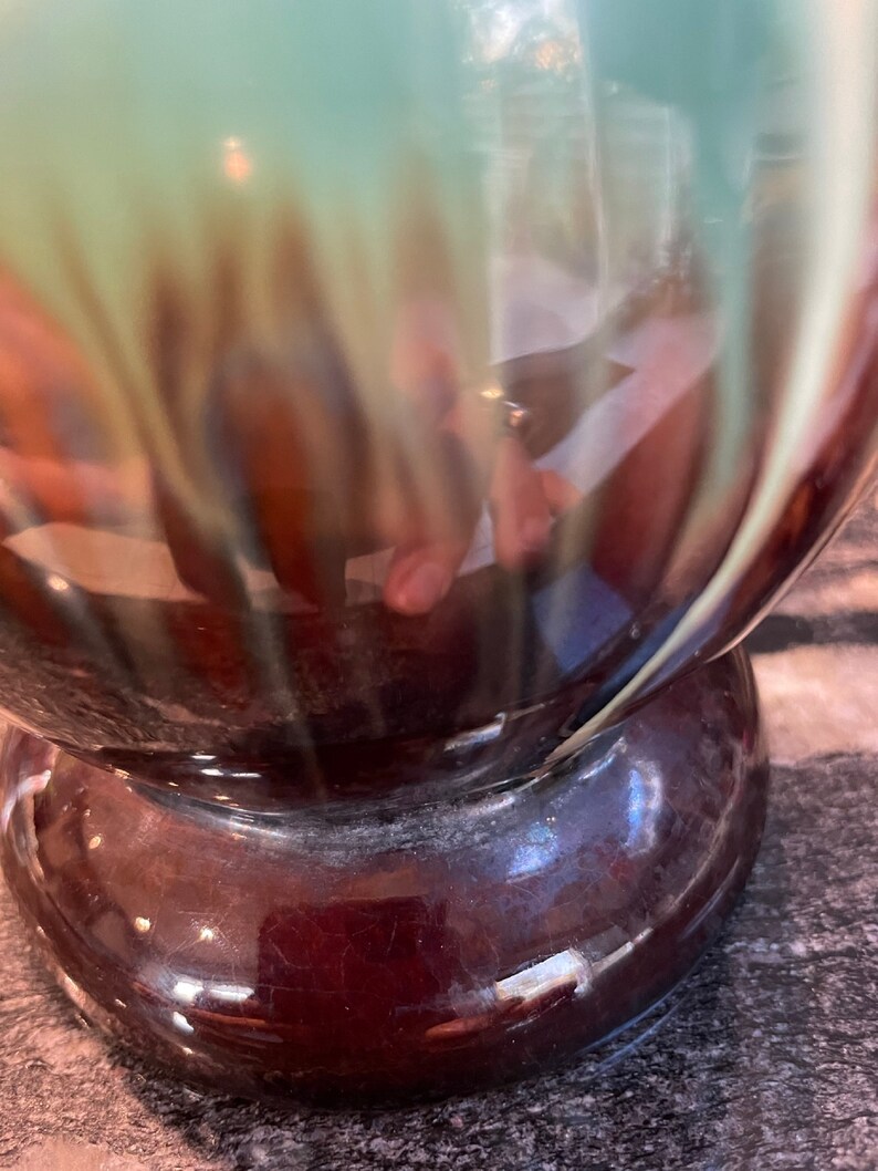 May include: A ceramic vase with a brown and green glaze. The vase has a rounded body and a wide base.