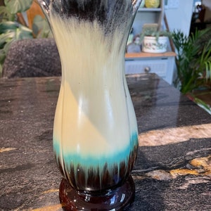 May include: A ceramic vase with a white, blue, and brown glaze. The vase has a wide mouth and a narrow base.