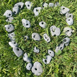 Könnte beinhalten: Eine Sammlung grauer, glatter, herzförmiger Steine mit einem Loch in der Mitte, die in Herzform auf einem Bett aus grünem Gras angeordnet sind.