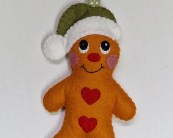 May include: A felt gingerbread man Christmas ornament. The orange figure has a green and white hat, rosy cheeks, and two red heart accents. It hangs from a green ribbon with white polka dots. A festive holiday decoration.