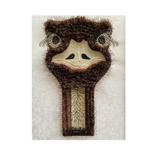 Op de afbeelding: Een bruin en beige geborduurde patch van een struisvogelkop met een pluche textuur. De struisvogel heeft zwarte ogen en een lange nek.