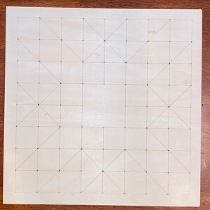 May include: A white wooden board with a grid pattern of squares and triangles drawn on it. The board is used for playing a game.