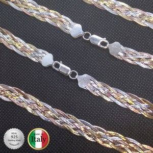 May include: Three silver chains with a braided design, featuring a mix of silver, gold, and rose gold tones. The chains are connected with silver clasps. The image includes a circular label with the text "REAL 925 Sterling Silver GUARANTEE" and a second label with the text "MADE IN Italy".