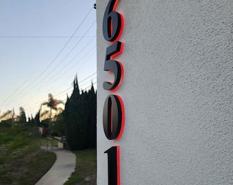 Puede incluir: Números de casa negros con contorno rojo, los números son 6501, montados en una pared blanca.