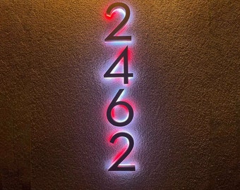 Puede incluir: Un primer plano de un letrero de número de casa con los números 2462 mostrados en negro sobre un fondo blanco. Los números están iluminados con luces rojas y blancas.