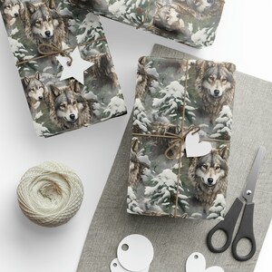 Op de afbeelding: Cadeaupapier met een gedetailleerde illustratie van wolven in een besneeuwd bos. Het papier is vastgebonden met touw en versierd met witte ster- en hartvormige labels. Een kluwen touw en een schaar zijn ook zichtbaar.