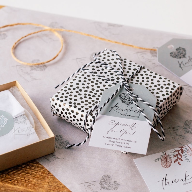 May include: A small gift box wrapped in white paper with black polka dots. A white tag with black text reads "Kindred Keepsakes Especially for You! Treasured Moments Captured in Every Keepsake".