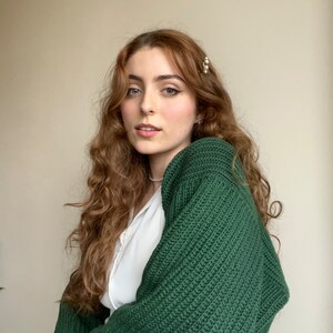 K&ouml;nnte beinhalten: Eine Frau mit langen, lockigen, rotbraunen Haaren tr&auml;gt einen dunkelgr&uuml;nen Strickcardigan. Sie tr&auml;gt ein wei&szlig;es Hemd unter dem Cardigan.