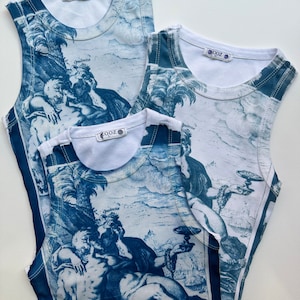 May include: Three white tank tops with a blue and white print of a reclining figure with a crown and a chalice. The tank tops have a ribbed texture and a small tag with the word "ZOZ" on the front.