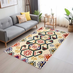 May include: A cream-colored rug with a geometric pattern in shades of red, blue, green, and yellow. The pattern features intricate designs and shapes.