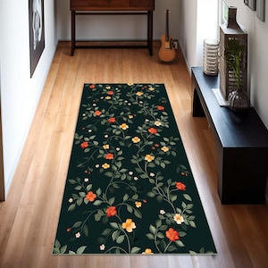 May include: A dark green runner rug with a floral pattern featuring orange and yellow flowers. The rug is placed on a wooden floor in a hallway.