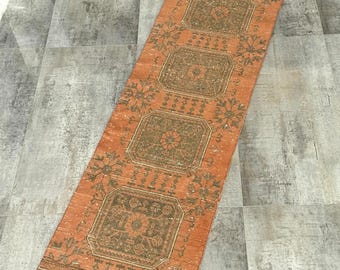 Puede incluir: Una alfombra corredora naranja con un diseño rectangular. La alfombra presenta un patrón repetitivo de formas geométricas y motivos florales en tonos marrones y beige. La alfombra es rectangular y parece estar hecha de material tejido.