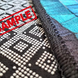 Puede incluir: Primer plano de una tela con estampado blanco y negro con un sello rojo "SAMPLE". La tela est&aacute; cosida a una tela con estampado azul y negro.