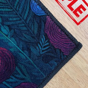 Puede incluir: Primer plano de una tela azul oscuro con un borde negro. La tela tiene un patr&oacute;n floral en tonos de morado, azul y verde.