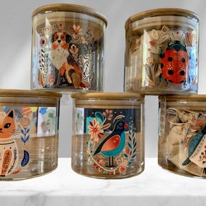 May include: Five glass jars with bamboo lids, each featuring a different illustrated design. The designs include a cat, a dog, a ladybug, a bird, and a bird with a flower. The jars are perfect for storing small items like tea, coffee, or spices.