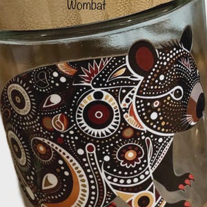 May include: A clear glass jar with a bamboo lid featuring a printed graphic of a wombat. The wombat is decorated with intricate dot patterns in shades of black, white, brown, and red. The word Wombat is printed in black text on the lid.