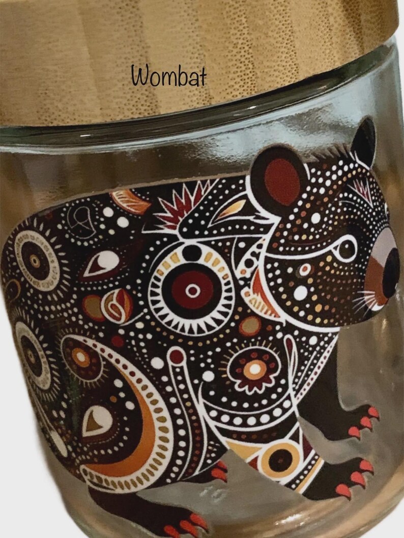 May include: A clear glass jar with a bamboo lid featuring a printed graphic of a wombat. The wombat is decorated with intricate dot patterns in shades of black, white, brown, and red. The word Wombat is printed in black text on the lid.