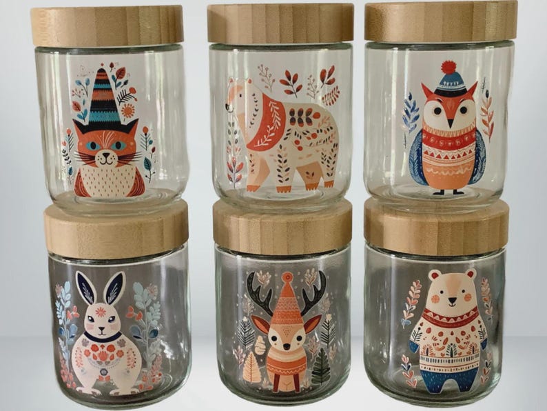 May include: Six clear glass jars with light brown wooden lids, arranged in two rows of three. Each jar features a colorful illustration of a woodland animal, including a cat, bear, owl, rabbit, deer, and another bear, all decorated with floral patterns.