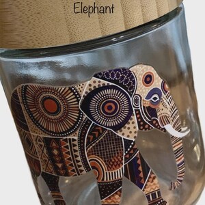 May include: A clear glass storage jar with a light brown bamboo lid. The word Elephant is printed on the lid. The side of the jar features a detailed graphic of an elephant decorated with intricate geometric patterns in shades of brown, orange, and black.
