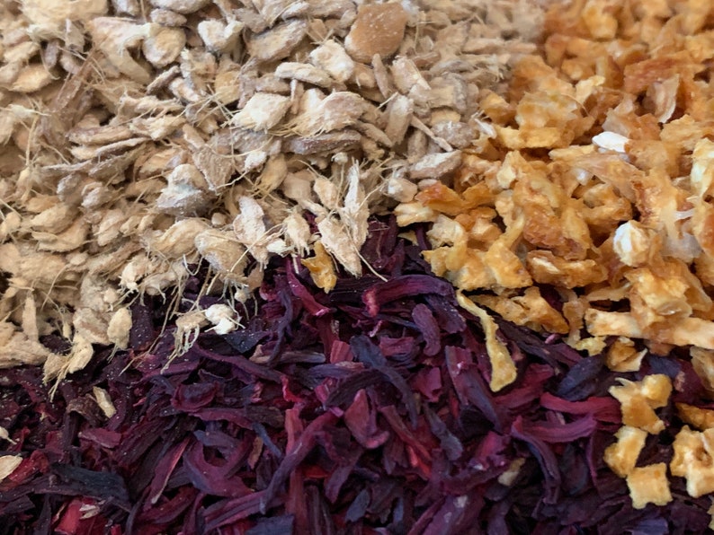 May include: A close-up of a mixture of dried herbs and spices. The mixture includes light brown ginger, orange peel, and dark red hibiscus.