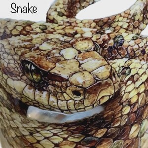 May include: A detailed illustration of a coiled snake with brown, tan, and yellow scales. The snake has a prominent head with visible eyes and nostrils. The word Snake is printed in black text in the upper left corner of the image.