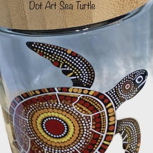 May include: A clear glass jar with a light-colored bamboo lid featuring a dot art sea turtle design in shades of red, orange, yellow, and black. The text Dot Art Sea Turtle is printed in black on the upper portion of the glass jar surface.