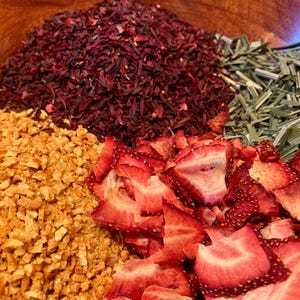 May include: A wooden bowl filled with dried fruit and herbs for making tea. The bowl contains dried hibiscus, dried ginger, dried strawberries, and dried lemongrass.