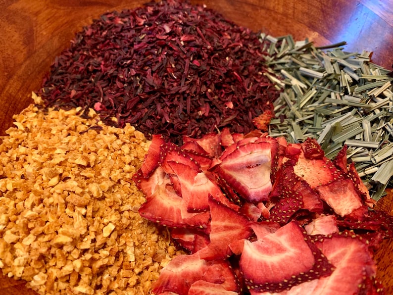 May include: A wooden bowl filled with dried fruit and herbs for making tea. The bowl contains dried hibiscus, dried ginger, dried strawberries, and dried lemongrass.
