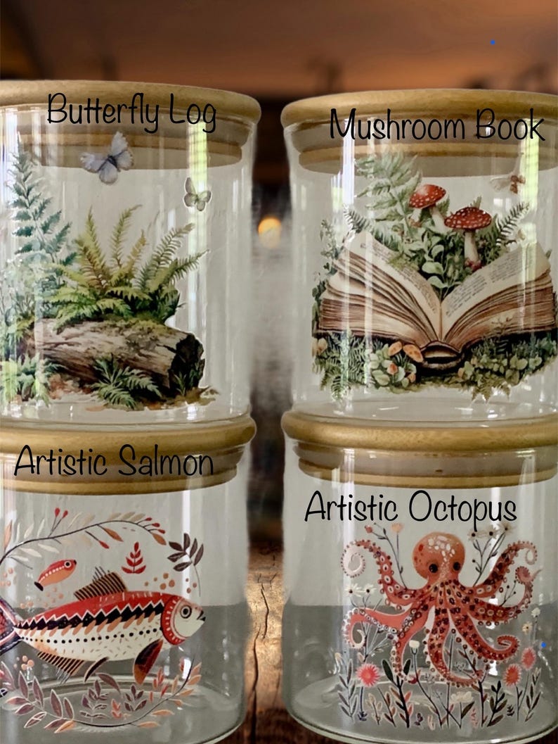 May include: Four clear glass storage jars with light wood lids. The top left jar features a log, ferns, and butterflies labeled Butterfly Log. The top right jar shows an open book with mushrooms labeled Mushroom Book. The bottom left jar displays a patterned fish labeled Artistic Salmon, and the bottom right jar shows an octopus and plants labeled Artistic Octopus.