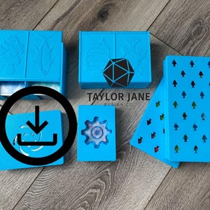 Könnte beinhalten: Mehrere hellblaue Boxen mit verschiedenen Designs, darunter Fische, ein Zahnrad und ein D20-Würfel. Eine Box ist geöffnet und zeigt eine Schublade. Die Boxen sind auf einer Holzoberfläche angeordnet. Der Text "TAYLOR JANE DESIGN CO." ist sichtbar.