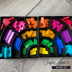 May include: A black plastic storage box with compartments filled with colorful plastic blocks. The blocks are in various shapes and sizes, including squares, rectangles, and L-shapes. The colors of the blocks are red, orange, yellow, green, blue, purple, and pink.