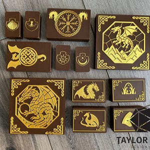 May include: Brown and gold decorative boxes with various designs, including dragons, shields, and Celtic knots. The boxes are arranged on a wooden surface. The boxes are rectangular and square, with gold-colored designs.