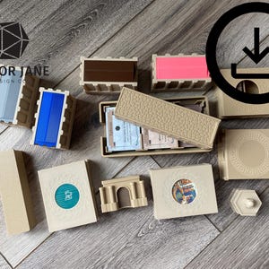 Puede incluir: Un conjunto de componentes de juego de cartas de color beige, marrón y azul, que incluye un porta tarjetas, un pequeño arco y una ficha redonda con un diseño circular. Los componentes están dispuestos sobre una superficie de madera.